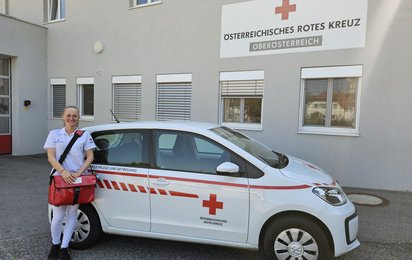 Melita Halilic ist in der Mobilen Pflege im Bezirk Linz-Land tätig. Am Bild sieht man sie, wie sie vor einem Auto der Mobilen Pflege steht.