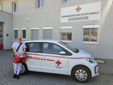 Melita Halilic ist in der Mobilen Pflege im Bezirk Linz-Land tätig. Am Bild sieht man sie, wie sie vor einem Auto der Mobilen Pflege steht.