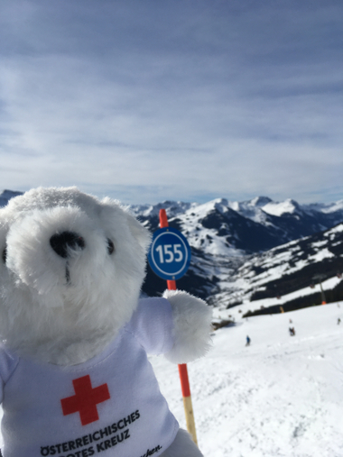 Bärli steht vor einer runden blauen Tafel mit einer Nummer darauf. Sie kennzeichnet eine bestimmte Piste im Skigebiet und dient der Orientierung.