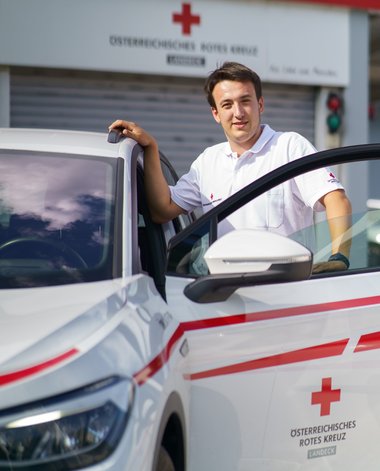 Ein Rotkreuz-Mitarbeiter in Uniform steigt in eine Rotkreuz-Auto ein