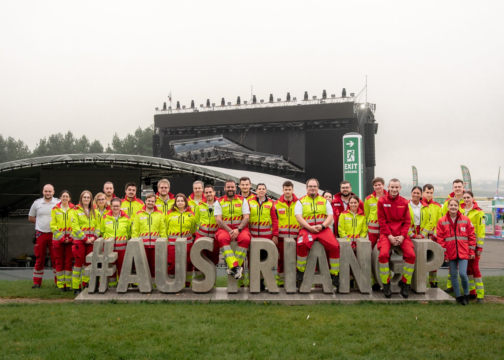 Ein Team an Sanitäter:innen steht hinter einem Schriftzug "#AustrianGP". Sie tragen Rotkreuz-Uniform und sind im Zuge des MotoGP-Rennens am Red Bull Ring im Einsatz.