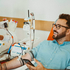 Junger Mann beim Blutspenden mit Brille, Tattoos und Handy
