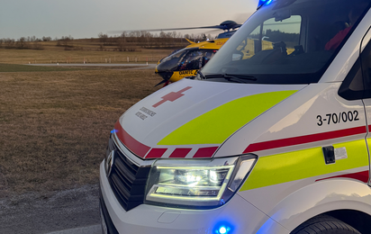 Ein Rettungstransportwagen der Rotkreuz-Bezirksstelle Waidhofen/Thaya steht bei einem Einsatz mit Blaulicht direkt neben einem Feld.