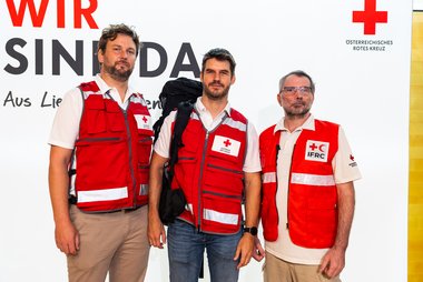 Drei Delegierte des Roten Kreuzes in Unifrom vor einer Pressewand