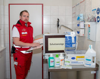 Patrick Peinhaupt - Bezirkshygienebeauftragter - steht in Rotkreuz-Einsatzuniform in einer Hygieneschleuse und stellt Equipment zur Desinfektion vor.