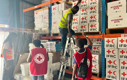 Lager für Hilfsgüter in Jamaika, Kartons mit IFRC Logo und Mitarbeiter auf Leiter