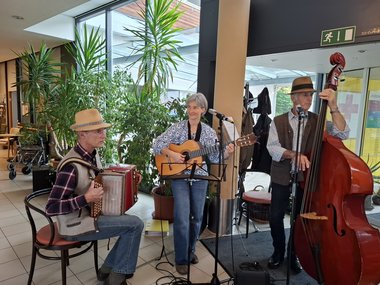 Musikgruppe, die das Fest begleitete. Links ein sitzender Mann mit Hut an der Ziehharmonika, in der Mitte eine stehende Frau mit Gitarre, recht ein stehender Mann mit Hut und Kontrabaß
