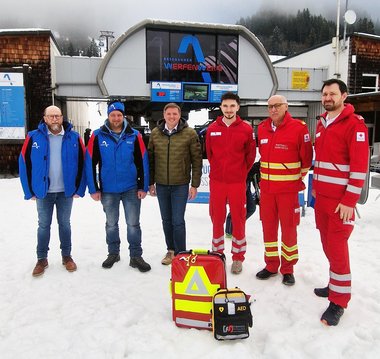 Gruppenfoto mehrerer Männer im Schnee vor einem Gebäude der Bergbahnen Werfenweng, davor stehen ein Notfallrucksack und ein Defibrillator.