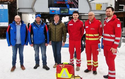 Gruppenfoto mehrerer Männer im Schnee vor einem Gebäude der Bergbahnen Werfenweng, davor stehen ein Notfallrucksack und ein Defibrillator.