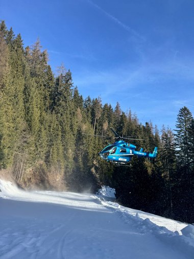 Ein blauer Notarzthubschrauber hebt von einem Ziehweg im Skigebiet Wildkogel ab.
