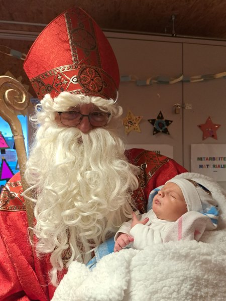 Der Nikolaus hält ein Baby in der Hand und lächelt in die Kamera.