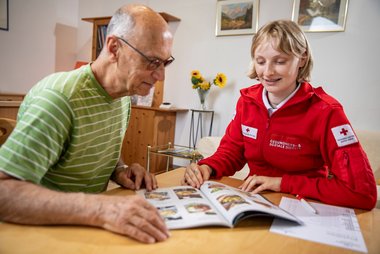 Eine Rotkreuz-Mitarbeiterin und ein älterer Herr scheuen sich die Speisen Auswahl an....