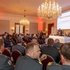 Festsaal mit Gästen und Redner:innen auf einer Bühne