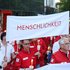 Rotkreuzler:innen tragen ein Banner mit dem Grundsatz "Menschlichkeit"