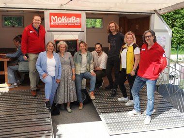 Eine Gruppe von Menschen steht unter dem Vordach eines Anhängers.