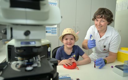 Weltblutspendetag - © Credit: OÖRK/Hofer Eine Labor-Mitarbeiterin zeigt einem Kind wie man in der Blutzentrale arbeitet.