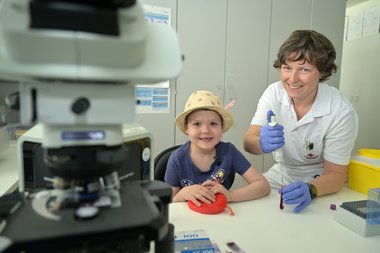 Eine Labor-Mitarbeiterin zeigt einem Kind wie man in der Blutzentrale arbeitet.