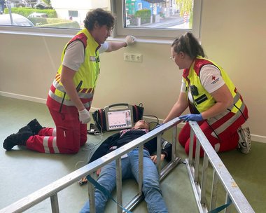 In einem Übungsszenario wurde die Versorgung nach einem Sturz aus großer Höhe geübt. Eine Person liegt am Boden, die Beine in einer Leiter verkeilt. Daneben knien zwei Sanitäterinnen.