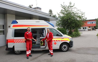 Ein Rettungsauto und davor stehen ein Vater mit seinem Sohn. Alfons und Andreas.