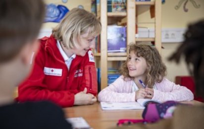 Rotkreuzmitarbeiterin, die ein Mädchen beim Lesen unterstützt