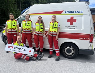 Mitarbeiterinnen der Dienststelle Hof vor einem Rettungswagen. Vier stehen, einer sitzt vor den anderen und hält ein Schuld mit der Aufschrift "Wir sind da".