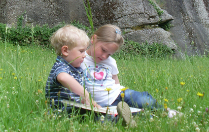 Zwei Kinder sitzen in der Wiese vor der Kinderburg Rappottenstein und lesen ein Buch.