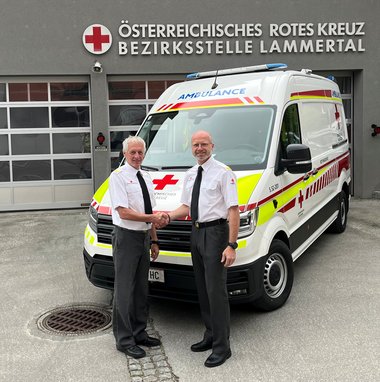 Zwei Männer stehen vor einem Rettungswagen und schütteln die Hände