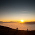 Man sieht einen farbenfrohen Sonnenuntergang, Wolken und einen Berghang.