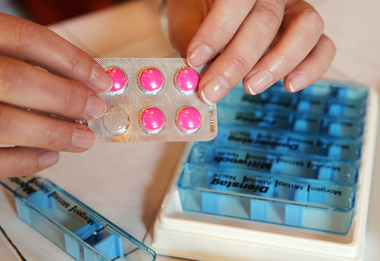 Zu sehen sind die Hände einer Frau, die Tabletten für eine andere nicht zu sehende Person portionieren