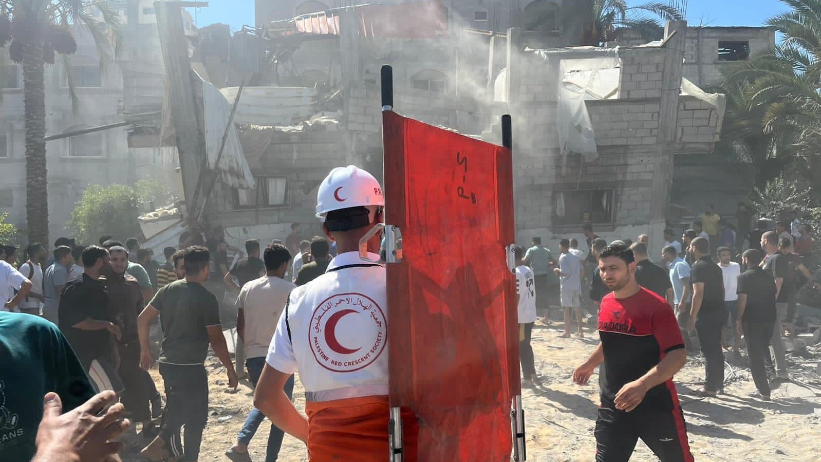 © Palestine Red Crescent Society Sanitäter mit einer Trage in der Hand steht vor einem zerstörten Gebäude