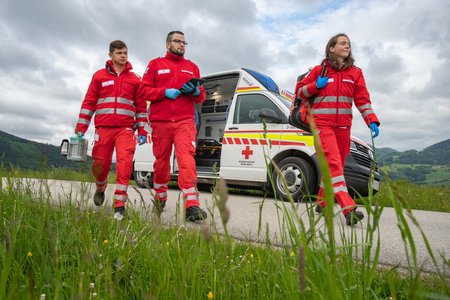 Drei Rotkreuz-Mitarbeiter:innen gehen von einem Rotkreuz-Fahrzeug weg in einen Einsatz