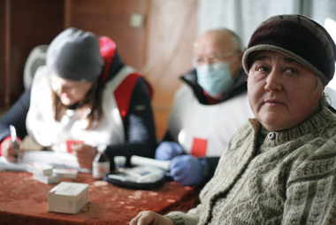 Ukraine, Nelipiwka, November 2019. Wera Parnizkaja sitzt in der mobilen Klinik des Roten Kreuzes. Seit 2014 herrscht hier ein bewaffneter Konflikt, der dazu führte, dass es in dieser Region keine Ärzte mehr gibt. Die einzige Versorgung, die es gibt, ist eine mobile Klinik, die das Rote Kreuz organisiert – mitfinanziert von der Österreichischen Agentur für Entwicklungszusammenarbeit (ADA). Zwei Mal im Monat kommen ein Arzt und zwei Pflegerinnen, die sich der PatientInnen annehmen. Sie bieten freie medizinische Behandlung und Medikamente. Querformat.