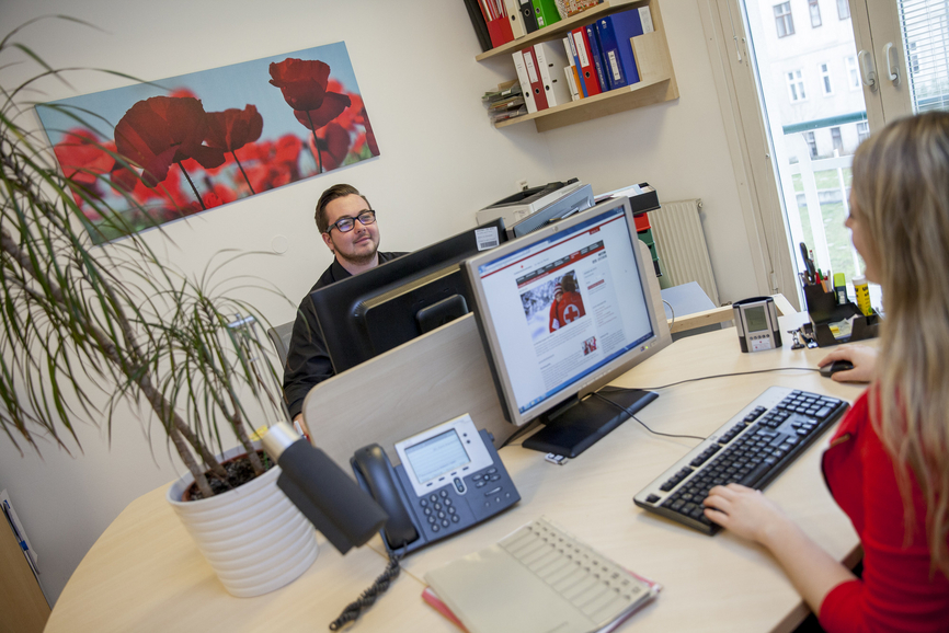 Mitarbeiten im Rechnungswesen - © Österreichisches Rotes Kreuz Markus Hechenberger ein junger Mann sitzt am Bürotisch vor dem Computer im Büro und ihm gegenüber eine junge Frau, die man von hinten sieht