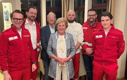 Ein Gruppenfoto mit Gitta Huber, ihrer Familie und Rettungsdienstmitarbeiter:innen aus Vöcklabruck