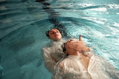 Ein Teilnehmer zieht einen anderen mit der Hand am Kinn durchs Wasser