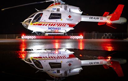 Der Notarzthubschrauber Martin 1 an seinem Stützpunkt bei Nacht spiegelt sich in einer Wasserpfütze.