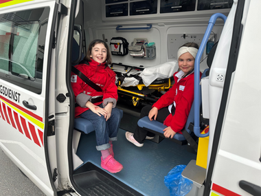 Jugendrotkreuzkinder sitzen in einem Krankentransportwagen bei geöffneter Türe.