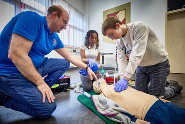 Zwei Schülerinnen des BRG Traun üben mit einem Lehrbeauftragten vom Roten Kreuz die Wiederbelebung an einer Simulationspuppe.