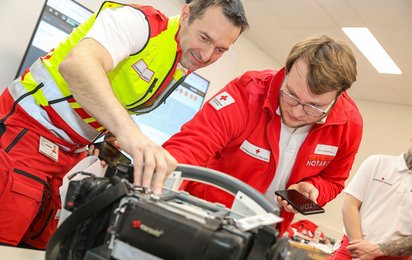 Links zu sehen ist Doktor Alexander Franz in einer Notarzt-Uniform mit Gilet, rechts ein Notarzt in Rotkreuz-Uniform. Beide betrachten ein Corpuls-Gerät zur Überwachung von Vitalparametern von Patientinnen.