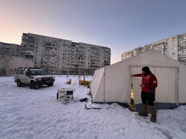 Ein Zelt und ein Rotkreuzauto vor einem Wohngebäude in der Ukraine, schneebedeckte Umgebung