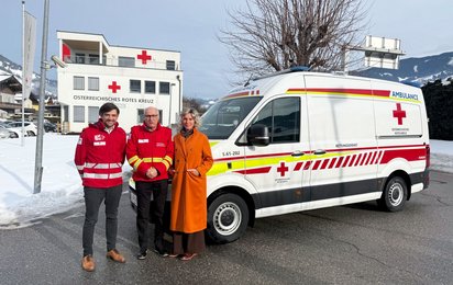 Drei Personen stehen vor einem Rettungswagen des Roten Kreuzes. Im Hintergrund ist die Rotkreuz-Bezirksstelle Sankt Johann zu sehen. Von links nach rechts: Daniel Kofler (Bezirksgeschäftsführer Rotes Kreuz St. Johann), Peter Riepler (Bezirksrettungskommandant St. Johann), Eveline Huber (Bürgermeisterin St. Johann)