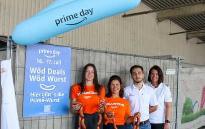 Mitarbeiter:innen von Amazon und der Team Österreich Tafel Graz-Stadt halten Wurstketten in den Händen.