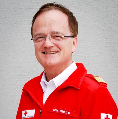 © Melanie Reiter Man sieht das Portraifoto eines Mannes mit kurzem, braunen Haar und Brille in einer roten Uniformjacke