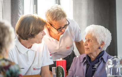 Seniorentreff_02 - © RK NÖ/Florian Schodritz Eine Rotkreuz-Mitarbeiterin unterhält sich mit sitzenden Senior_innen.
