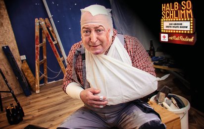 Rudi sitzt mit verbundenem Kopf und Arm mitten in einer Bausstelle.