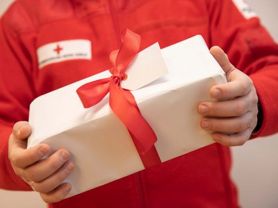 Ein männlicher RK Mitarbeiter in Uniform hält ein Weihnachtsgeschenk mit roter Schleife ins Bild.