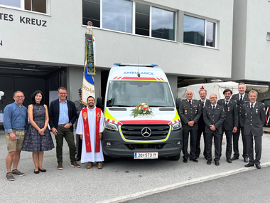 Bürgermeister, Vizebürgermeister, Pfarrer, Bezirksrettungskommandant, Bezirksrettungschefarzt und Bezirksrettungsstellvertreter, Bezirksgeschäftsführer, Abteilungskommandant und Abteilungskommandant-Stellvertreter stehen neben dem neu geweihten Rettungsauto