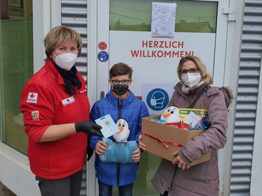 Rotkreuz-Markt-Mitarbeiterin übergibt vor dem Markt Eferding Weihnachtspakete an Kunden