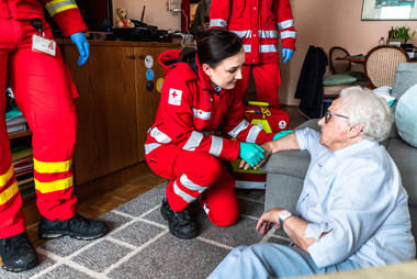 Eine Sanitäterin kniet neben einer gestürzten Frau, dahinter stehen weiter Sanitäter.