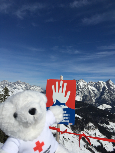 Bärli steht vor einer Tafel, die vor möglichen Lawinen warnt, falls die präparierten Pisten verlassen werden.
